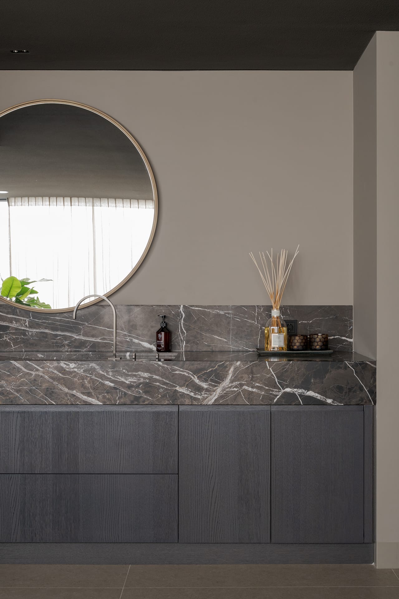 Wastafelblad en achterwand in marmer Havana Brown met een kraan van Dornbracht en een ronde spiegel in de wellness.