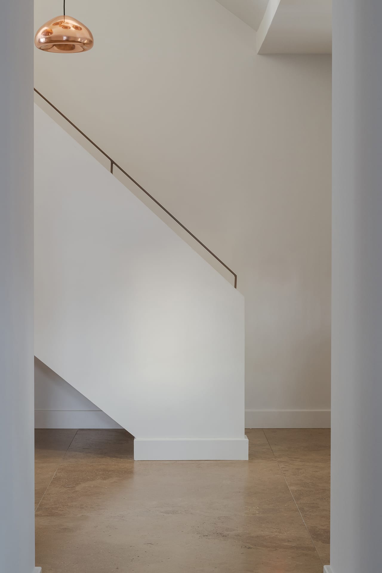 Wit gestucte trap met een smalle leuning en een koperen hanglamp Void van Tom Dixon.