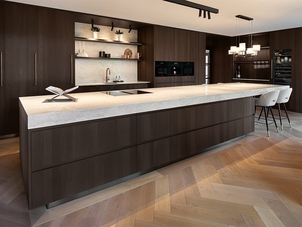 Arclinea Convivium kookeiland in Fume Oak met werkblad in kwartsiet Taj Mahal op een visgraatvloer.