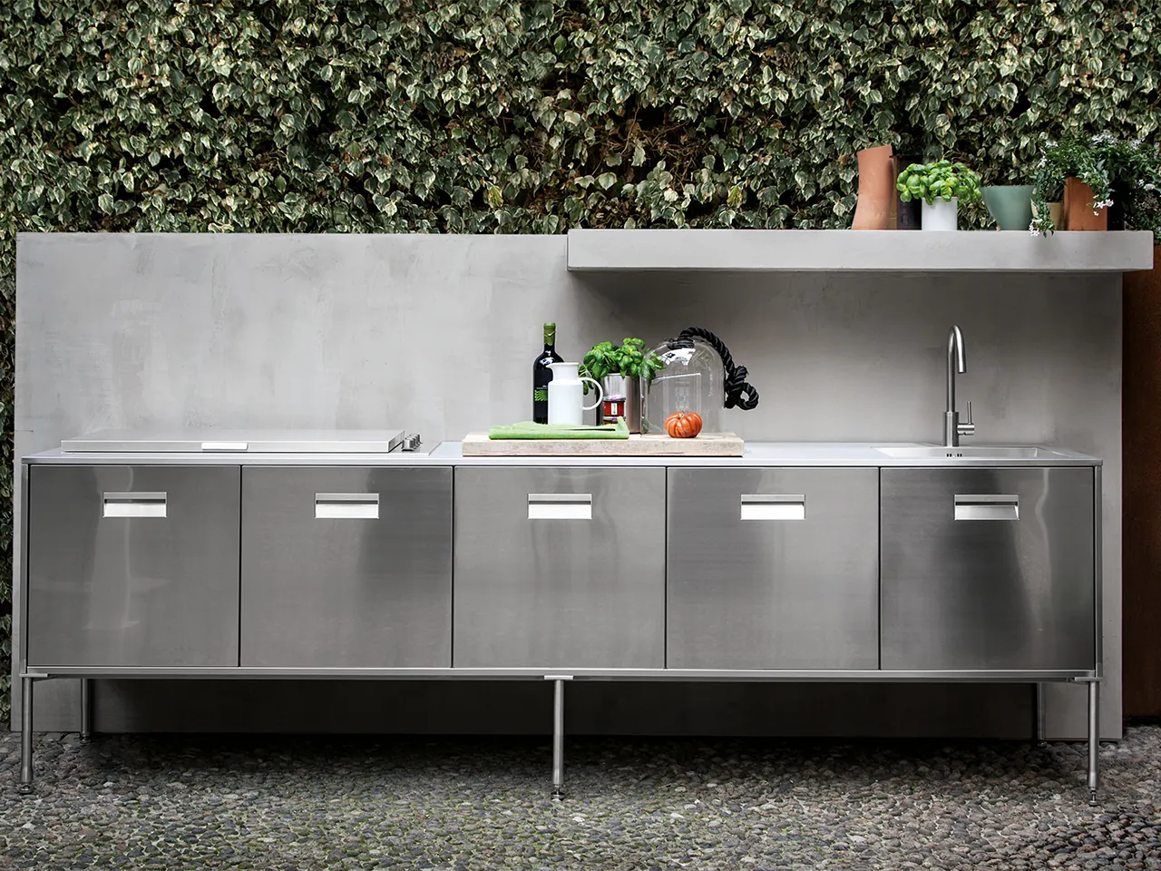 Arclinea Artusi Outdoor buitenkeuken in AISI 316 RVS op poten met spoelbak en werkblad tegen groene haag