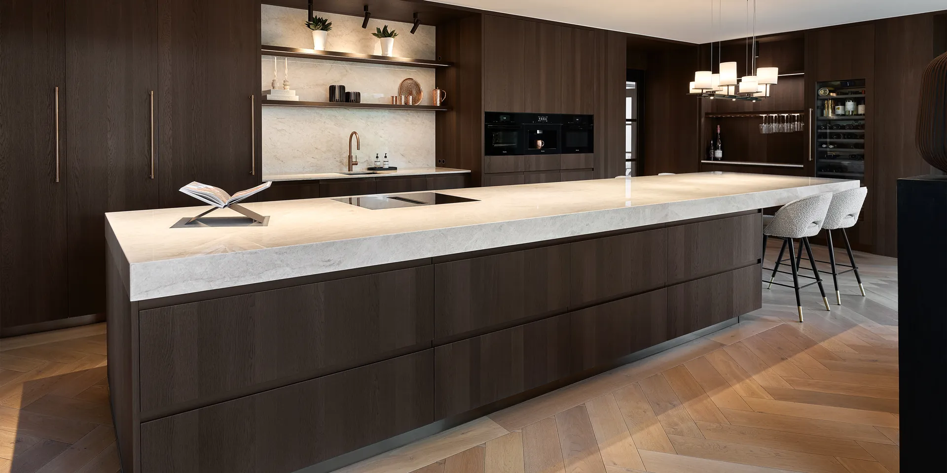 Arclinea Convivium kookeiland met aantafel in Fume Oak en kwartsiet Taj Mahal onder Kreon Cana railverlichting