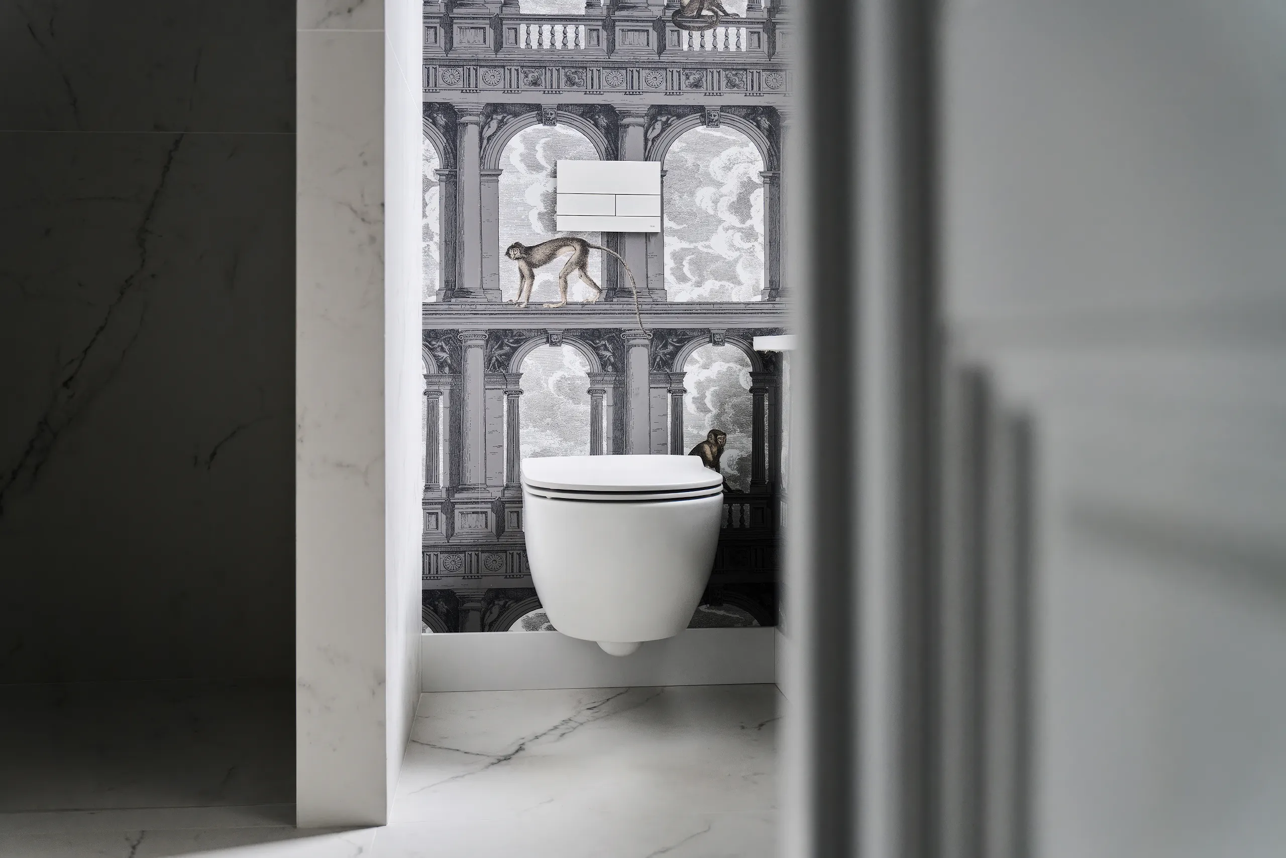 Badkamer met Fornasetti apenbehang keramische tegels in marmerlook Ceramica Flaminia toilet en TECE drukplaat artistiek Italiaans design